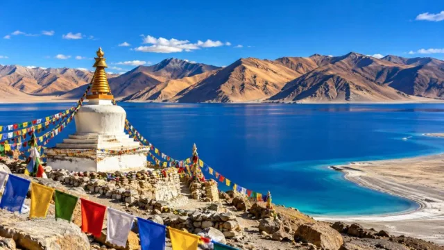 Blue Pangong Lake with golden Himalayan mountains and a stupa with prayer flags in Ladakh