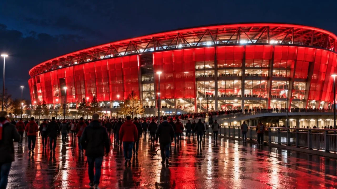 A brightly lit red football stadium exterior at night with fans walking towards it