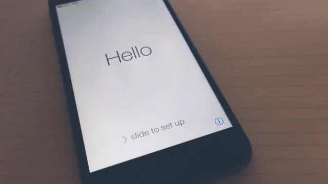 An iPhone lying on a table showing the Hello welcome screen with 'slide to set up' at the start of setup
