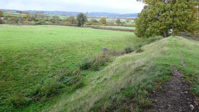 Grassy earthwork bank and ditch of Offa's Dyke running through green fields and autumn trees near Montgomery on the England-Wales border