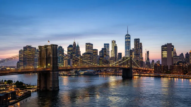 The Brooklyn Bridge and Manhattan skyline at dusk with city lights reflecting on the East River