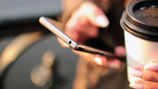 Close-up of hands using a smartphone while holding a takeaway coffee cup