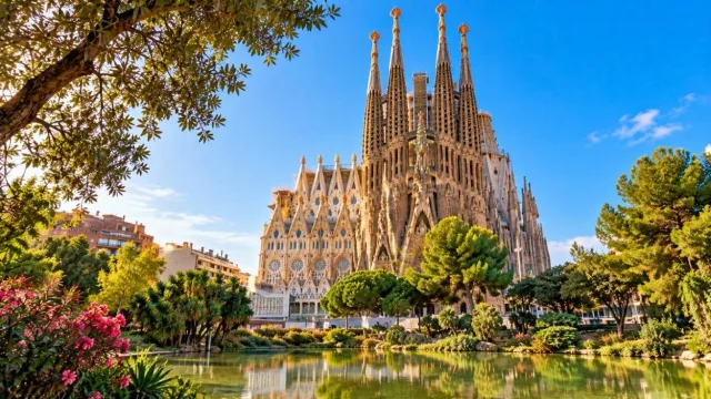 Sagrada Familia basilica towers against a blue sky, seen across a park pond