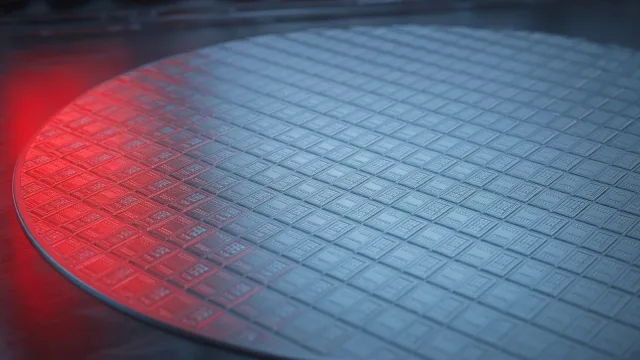 Close-up of a silicon wafer covered in chips, lit in blue with a red glow on one edge
