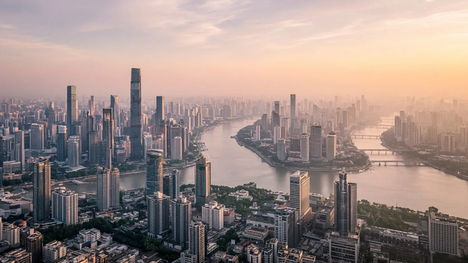 Aerial view of a modern financial district skyline beside a winding river in soft pink and gold dawn light
