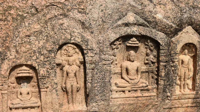 Weathered rock-cut reliefs of seated and standing Jain Tirthankaras carved in niches on a granite boulder at the Samanar Hills near Madurai