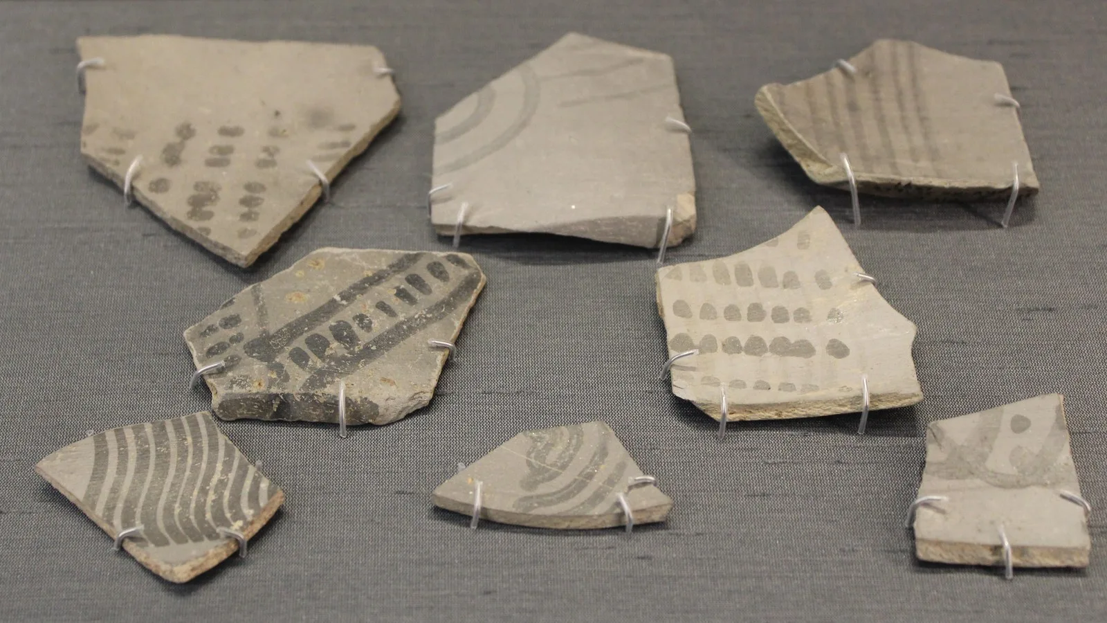 Fragments of Painted Grey Ware pottery from about 1000 BCE, light grey sherds painted with black dots, stripes and arcs, displayed on pins in the British Museum