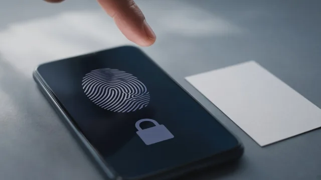 Fingertip above a phone showing a fingerprint symbol and a padlock, a blank card beside it