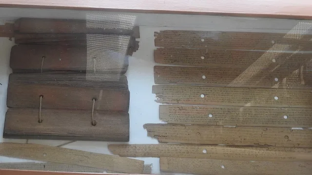 Bundles of palm-leaf manuscripts tied with cord and loose inscribed palm leaves in a glass display case